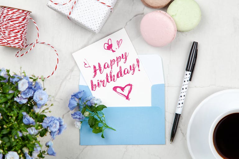 Celebratory birthday setup with a card, flowers, and coffee on a desk.
